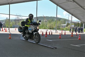 Zdjęcie. Policjant na motocyklu podczas konkurencji jazdy na motocyklu oraz inni umundurowani policjanci