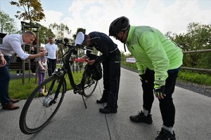 zdjęcie przedstawia policjanta montującego element odblaskowy na rowerze. Obok niego stoi kolarz.