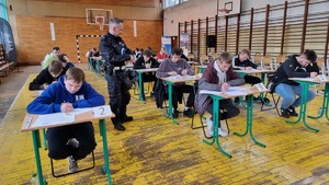 Uczniowie piszący test z wiedzy o przepisach ruchu drogowego. Nad przebiegiem testu czuwa policjant.