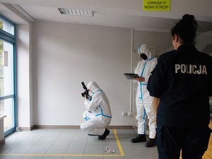 zdjęcie przedstawia policjantów w ochronnych kombinezonach wykonujących oględziny w pomieszczeniu