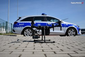 Na zdjęciu widoczny dron policyjny na tle zonakowane radiowozu wydziału ruchu drogowego.