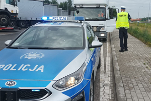 Na zdjęciu radiowóz oraz umundurowany policjant, który idzie w kierunku zaparkowanego za radiowozem samochodu ciężarowego.