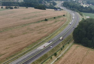 na zdjęciu widok z drona na drogę. na drodze widoczne samochody osobowe i ciężarowe.