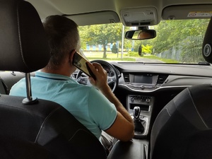 Na zdjęciu widoczny kierujący samochodem rozmawiający przez telefon trzymając go przy uchu.
