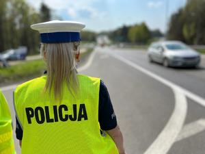 policjantka ruchu drogowego w kamizelce odblaskowej stojąca tyłem obserwuje ruch na drodze