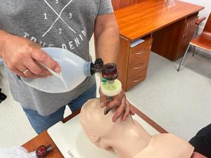 Zbliżenie na dłonie uczestnika szkolenia, który prowadzi wentylację pacjenta (fantom) za pomocą worka samorozprężalnego.
