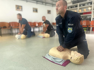Na pierwszym planie policyjny instruktor podczas prowadzenia masażu serca na fantomie. W tle widać pozostałych uczestników szkolenia.