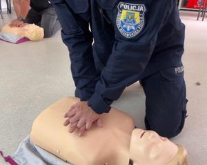 Zbliżenie na dłonie instruktora splecione na klatce piersiowej fantoma podczas wykonywania masażu serca przez policyjnego instruktora.