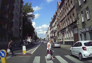 na zdjęciu widzimy kobietę przechodzącą przez przejście dla pieszych i przejeżdżający obok niej biały samochód