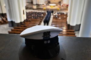 Widok z góry na uczestników uroczystości siedzących w katedrze - na pierwszym planie leży czapka policjanta z orkiestry