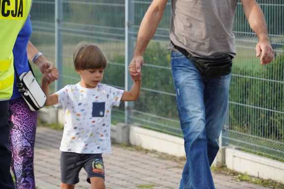 Chłopiec idący chodnikiem trzymając za rękę opiekuna.