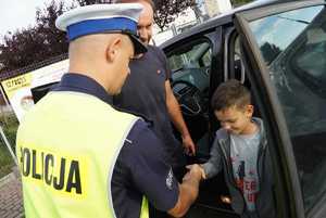 Policjant ruchu drogowego witający się z chłopcem, który przyjechał do przedszkola.