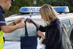 Policjant ruchu drogowego wręczający torbę z napisem &quot;Bezpieczny pieszy&quot; kobiecie.