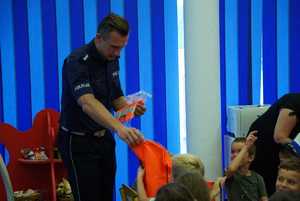 Policjant wręczający przedszkolakom odblaskowe worki na obuwie.