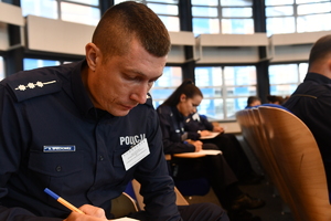 Policjant pochylony nad testem trzyma w ręce długopis