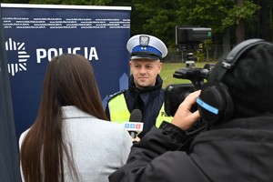 Policjant udzielający wywiadu telewizji TVS. Obok dziennikarka z mikrofonem oraz operator z kamerą.