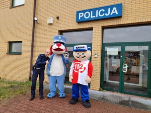 policjant ruchu drogowego z maskotką Sznupka i Ratusia stojący przed Komisariatem Autostradowym Policji w Gliwicach