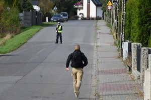 Zdjęcie. Policjant w mundurze i biegnący drogą mężczyzna