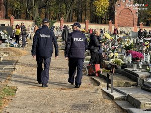 Zdjęcie przedstawia policjantów idących po cmentarzu