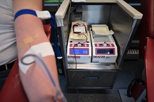 Na zdjęciu ręka mężczyzny oddającego krew, obok urządzenia, na których w workach widoczna jest pobierana krew.