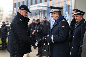 Grupa umundurowanych policjantów przed budynkiem komendy. Na pierwszym planie Komendant Wojewódzki Policji w Katowicach ściska dłoń policjanta