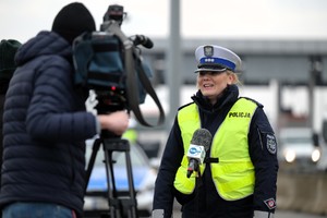 Zdjęcie przedstawia umundurowaną policjantkę w kamizelce odblaskowej przed kamerą.