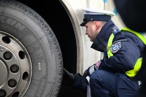 Zdjęcie przedstawia umundurowanego policjanta z dokumentami w ręku przeprowadzającego kontrolę autokaru.