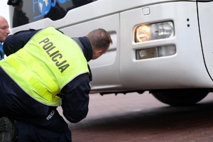 Zdjęcie przedstawia umundurowanego policjanta schylającego się przy autokarze.