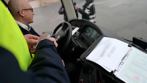 Zdjęcie przedstawia umundurowanego policjanta sprawdzającego dokumenty kierowcy autokaru.