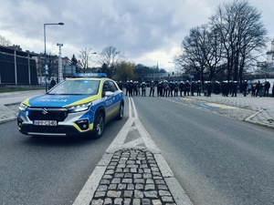 Umundurowani policjanci stojący na ulicy, a na pierwszym planie policyjny radiowóz