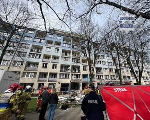Na zdjęciu blok mieszkalny, w którym doszło do wybuchu oraz policjant stojący przy parawanie strażackim.