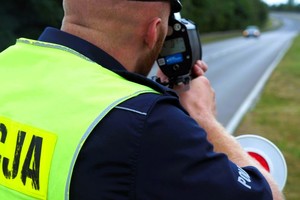 Na zdjęciu sylwetka policjanta ruchu drogowego mierzącego prędkość pojazdów