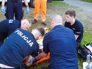 Na zdjęciu grupa policjantów udziela pierwszej pomocy poszkodowanemu, leżącemu mężczyźnie.