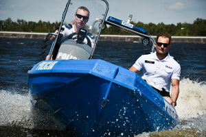 Na zdjęciu widać umundurowanych policjantów, patrolujących zbiornik wodny łodzią motorową z napisem policja.