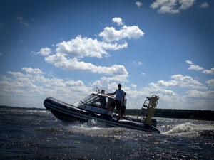 Na zdjęciu widać umundurowanych policjantów, patrolujących zbiornik wodny łodzią motorową z napisem policja.