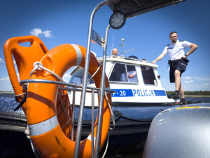 Na zdjęciu widać koło ratunkowe, a w tle umundurowanego policjanta, który stoi na łodzi motorowej.