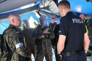 zdjęcie przedstawia rozmawiającą w namiocie grupę wojskowych z policjantem