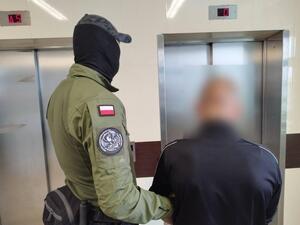 zdjęcie kolorowe: policjant stojący z zatrzymanym mężczyzna przed windą