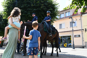 Kobieta z dziećmi stoi przy policjantach na koniach