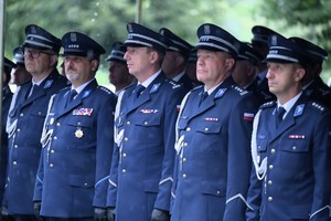 Policjanci w mundurach galowych podczas uroczystości stoją na zewnątrz budynku