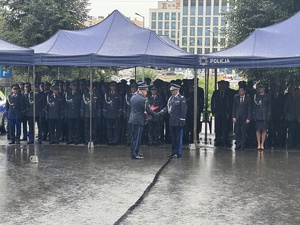 Policjanci wręczają generałowi upominek- w tle policjanci stojący pod namiotem