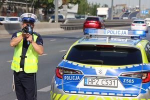 Na zdjęciu widać policjanta stojącego obok radiowozu mierzącego prędkość.