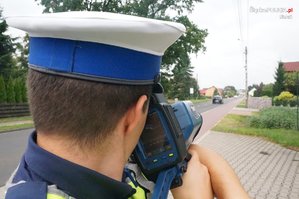 Zdjęcie kolorowe. Policjant z urządzaniem do pomiaru prędkości