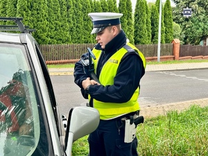 Zdjęcie kolorowe. Policjant stoi przy pojeździe