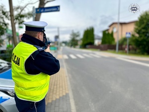 Zdjęcie kolorowe. Policjant z urządzaniem do pomiaru prędkości