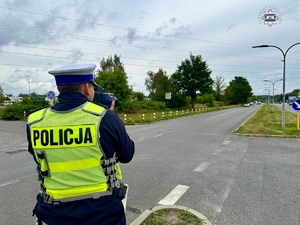 Zdjęcie kolorowe. Policjant z urządzaniem do pomiaru prędkości