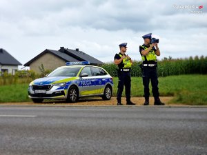 Zdjęcie kolorowe. Policjanci z urządzaniem do pomiaru prędkości