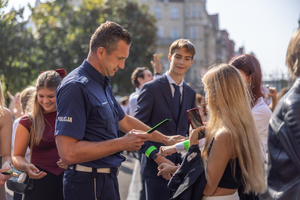 Umundurowany policjant w trakcie rozdawania opasek odblaskowych młodzieży.