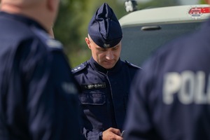 Na zdjęciu widoczny umundurowany policjant sprawdzający coś w telefonie komórkowym