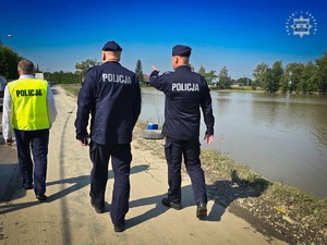 Na zdjęciu dwaj umundurowani policjanci idący wraz z trzecim w kamizelce odblaskowej